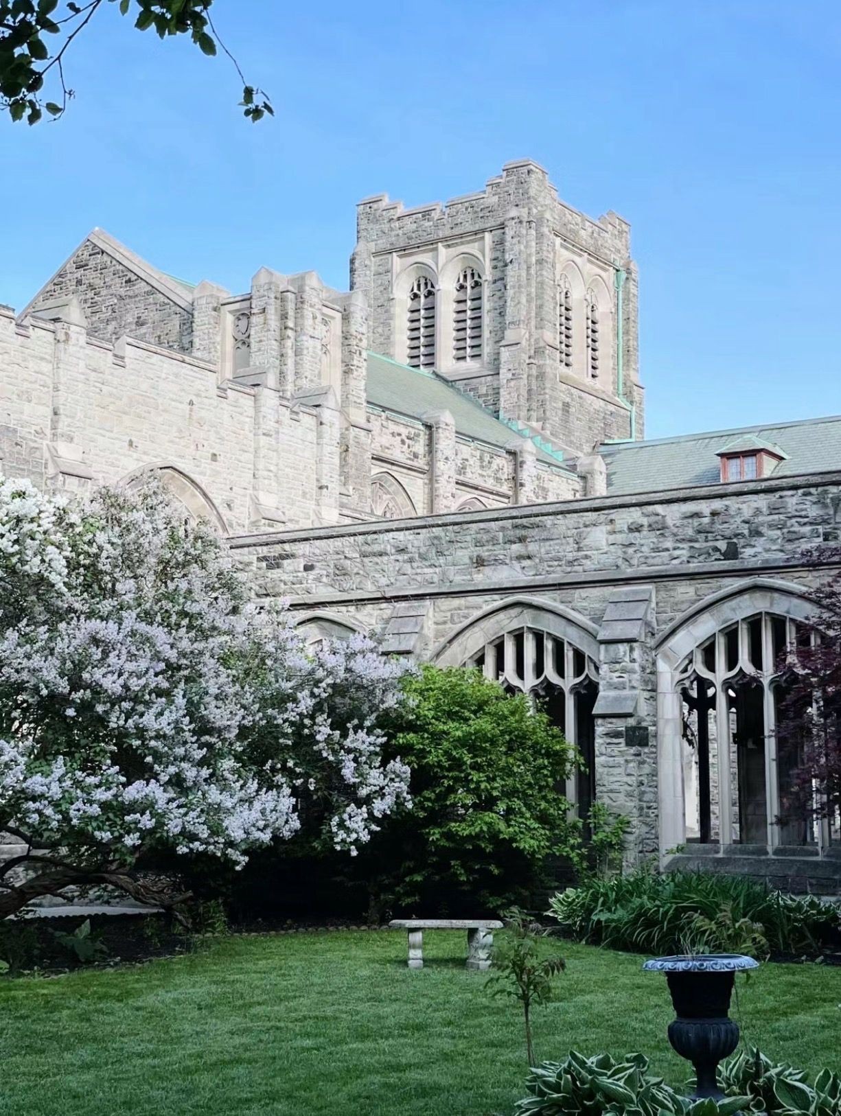 Stone church facade with arched windows overlooking a garden with blooming bushes and a stone bench.